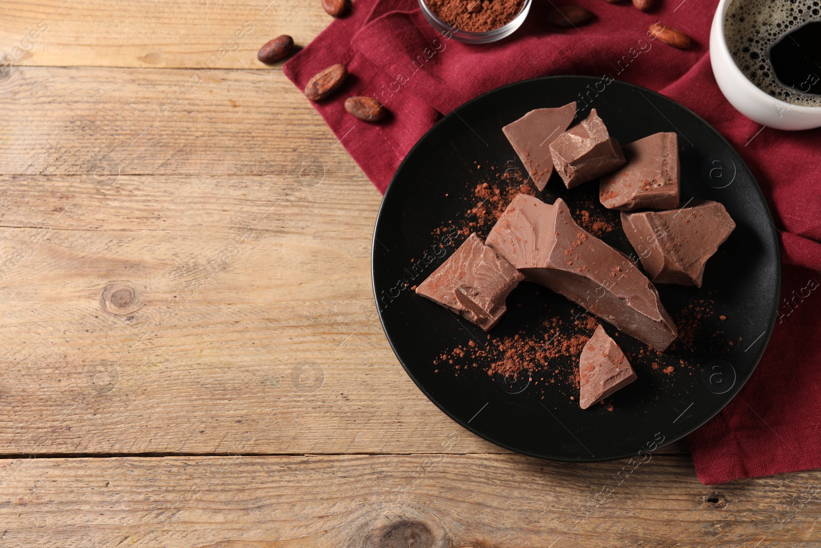 Photo of Pieces of tasty milk chocolate, cocoa beans and powder on wooden table, top view. Space for text