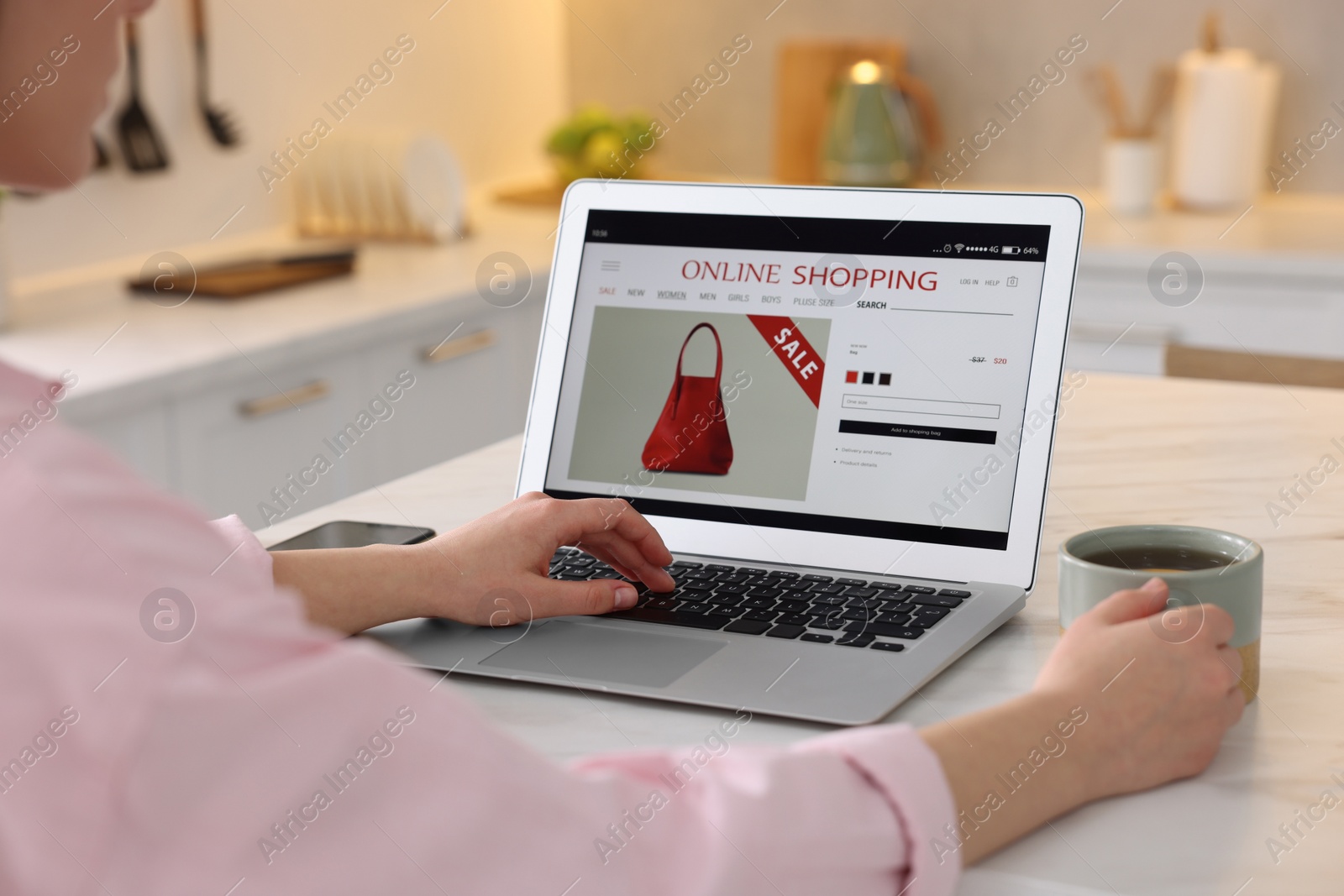 Photo of Woman with cup of tea shopping online during sale on laptop in kitchen, closeup