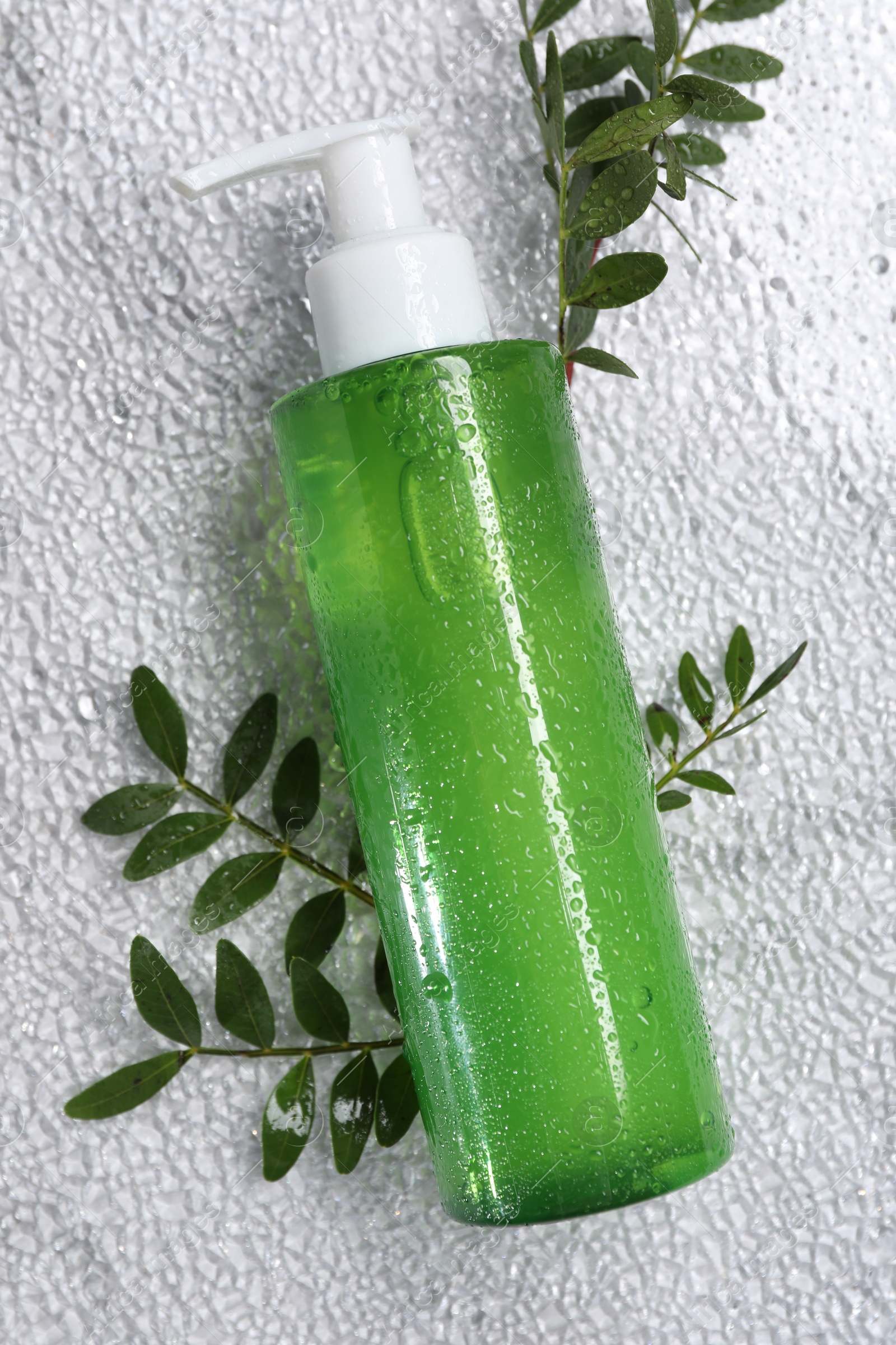 Photo of Bottle of face cleansing product and green leaves on white textured table, flat lay