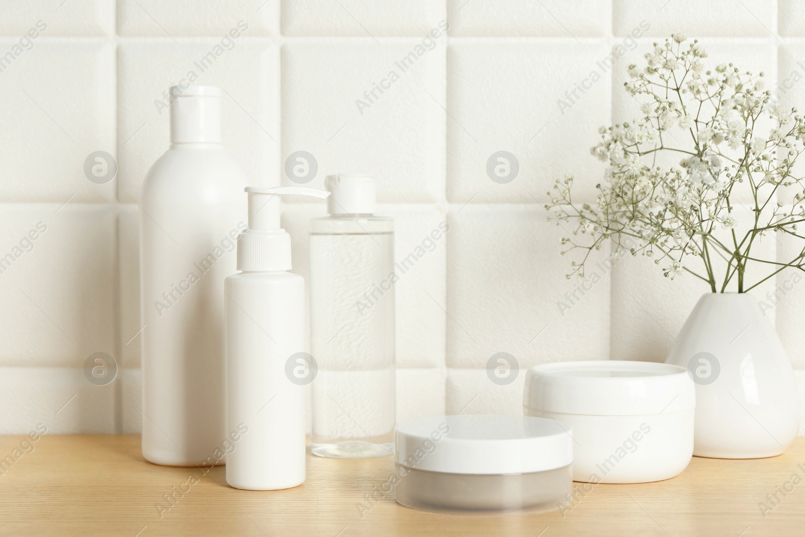 Photo of Bath accessories. Different personal care products and gypsophila flowers in vase on wooden table near white tiled wall