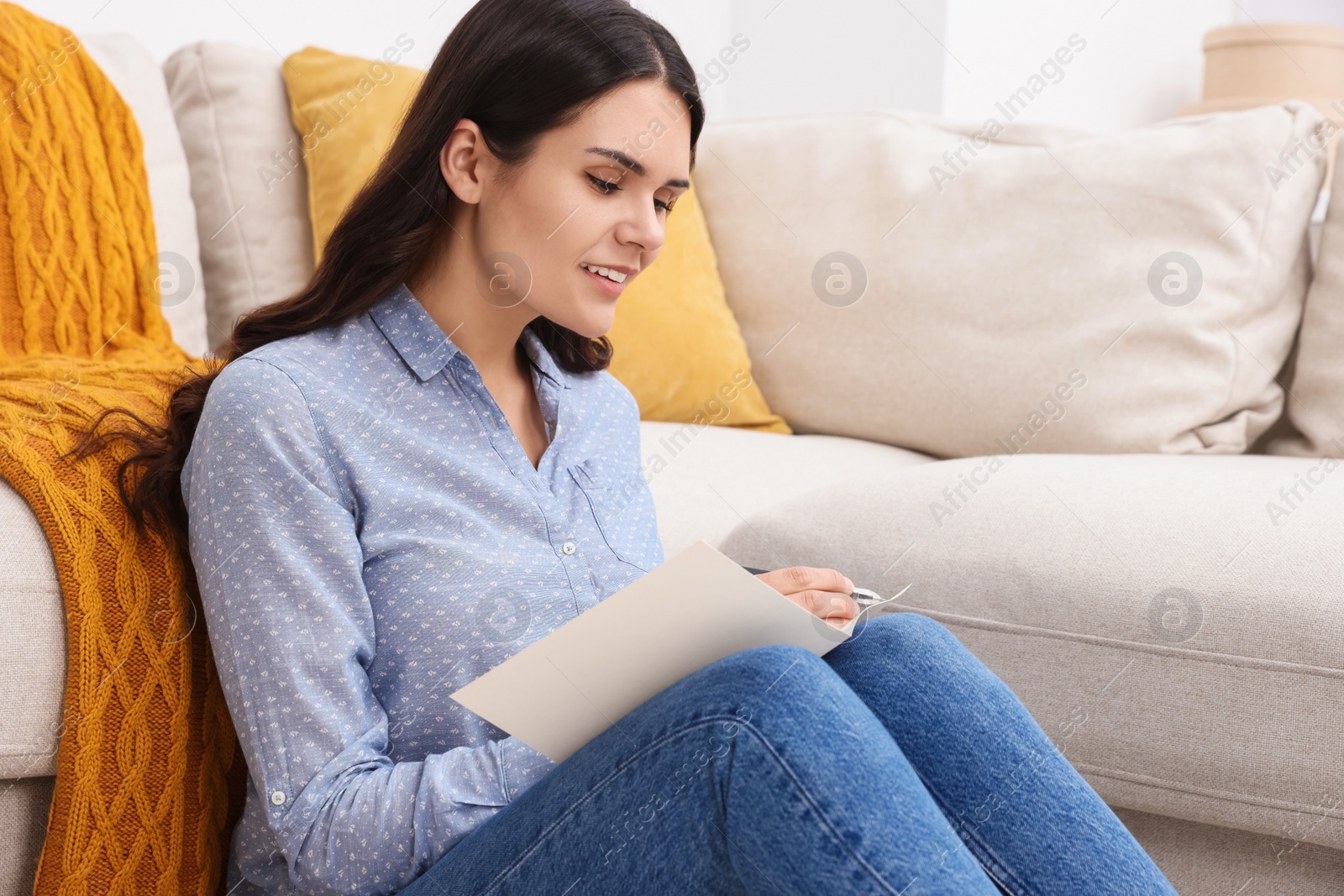 Photo of Young woman writing message in greeting card indoors