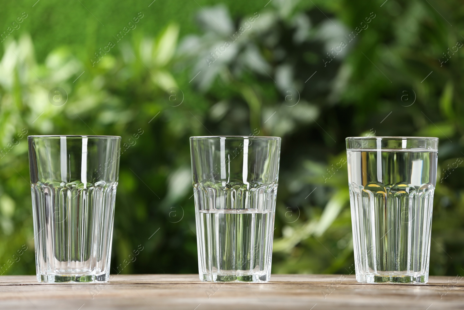 Photo of Empty, half and full glasses of water on wooden table against blurred background