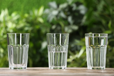 Empty, half and full glasses of water on wooden table against blurred background