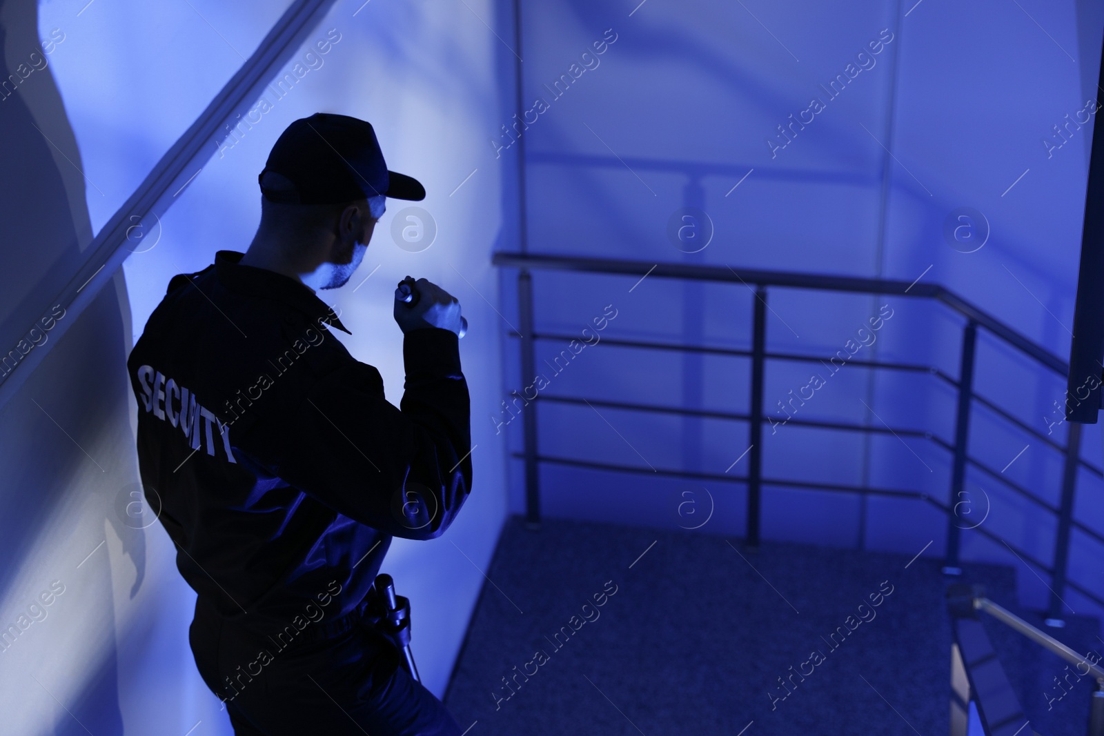 Photo of Male security guard with flashlight on stairs in darkness