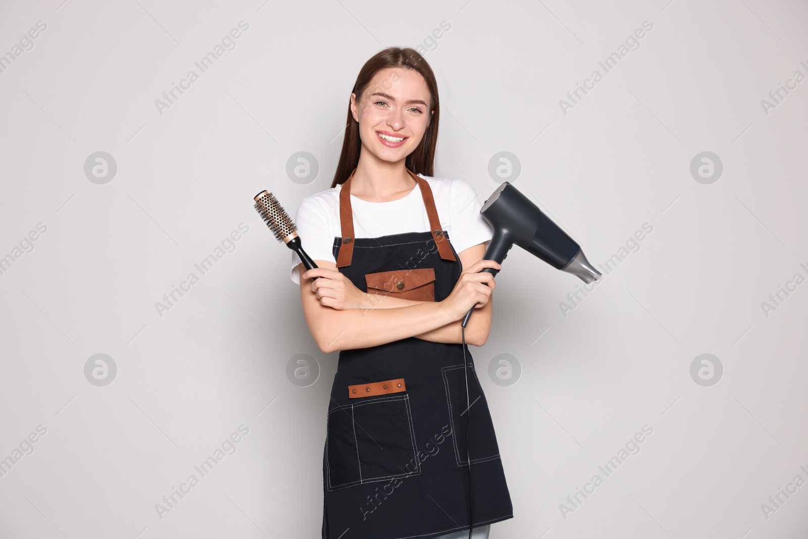 Photo of Portrait of happy hairdresser with hairdryer and brush on light background