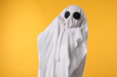 Photo of Creepy ghost. Person covered with white sheet on yellow background