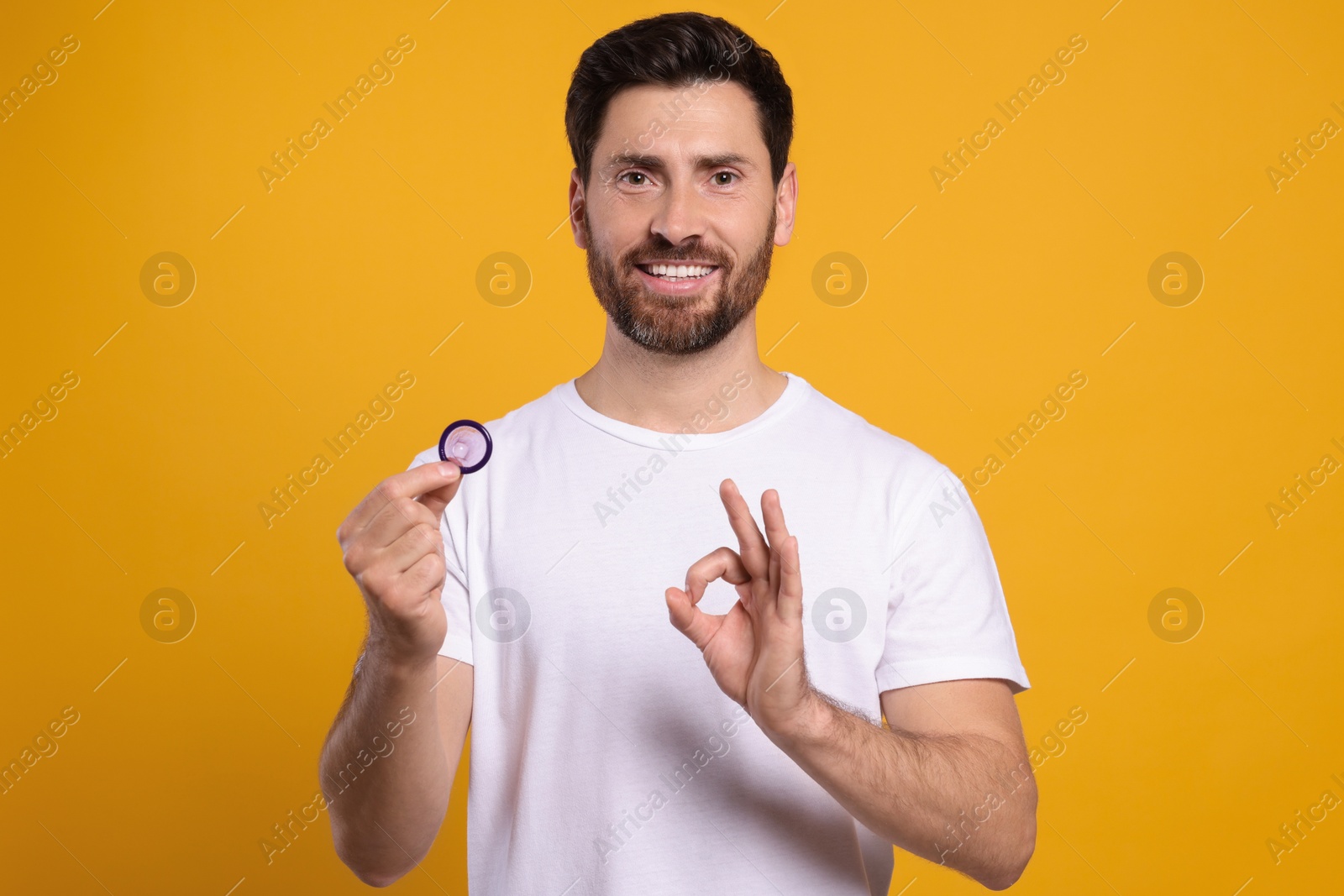 Photo of Happy man with condom showing ok gesture on yellow background. Safe sex