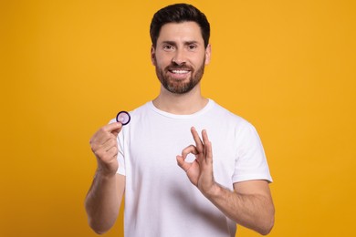 Photo of Happy man with condom showing ok gesture on yellow background. Safe sex