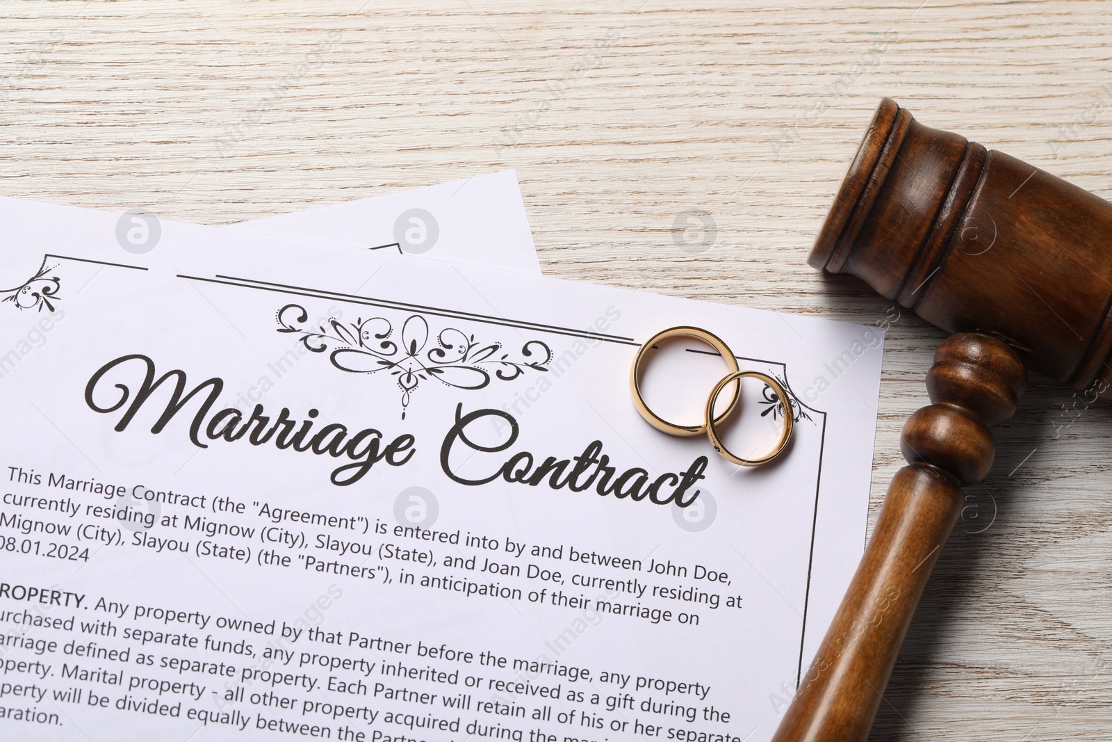 Photo of Marriage contract, golden wedding rings and gavel on wooden table, top view