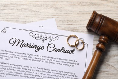 Photo of Marriage contract, golden wedding rings and gavel on wooden table, top view