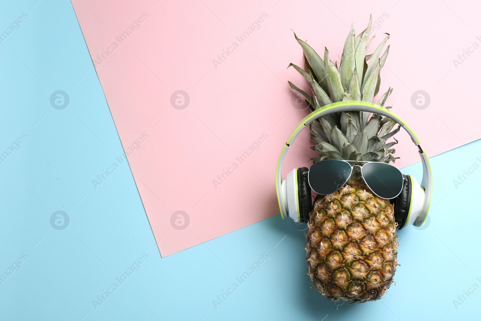 Photo of Top view of pineapple with headphones and sunglasses on color background, space for text. Creative concept