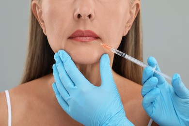 Photo of Doctor giving lips injection to senior woman on light grey background, closeup. Cosmetic surgery