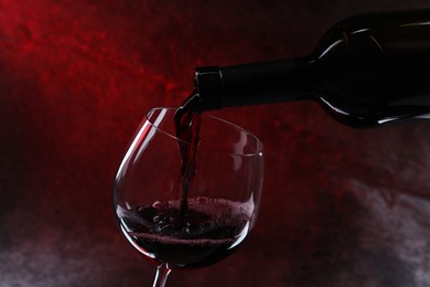 Pouring red wine from bottle into glass on color background, closeup