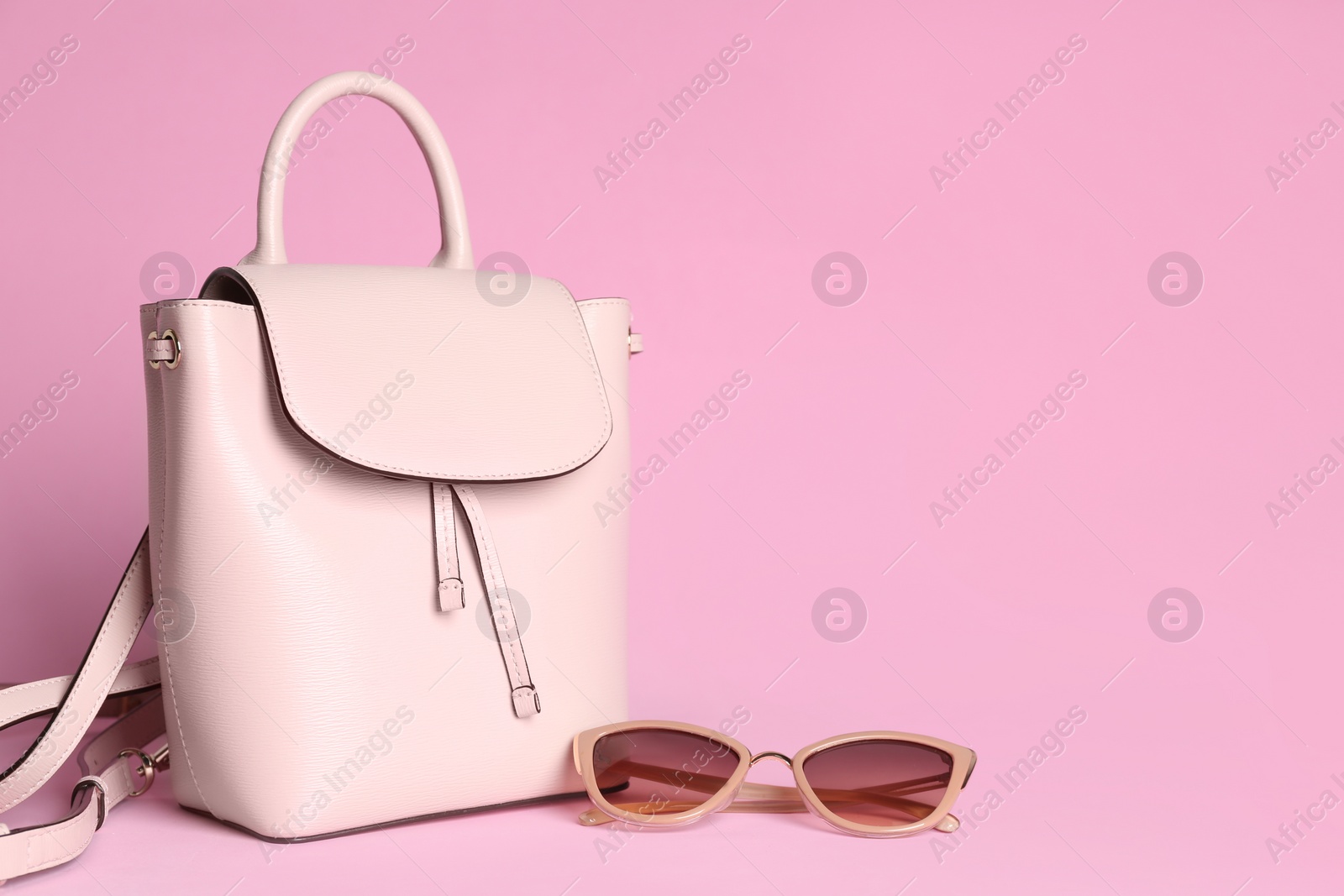 Photo of Stylish woman's backpack and sunglasses on light pink background. Space for text