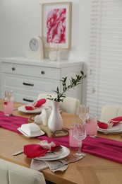 Photo of Color accent table setting. Glasses, plates, pink napkins and vase with green branch in dining room