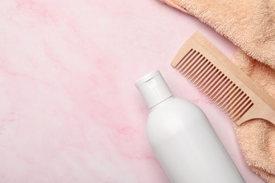 Photo of Shampoo bottle, wooden comb and towel on pink marble table, flat lay. Space for text