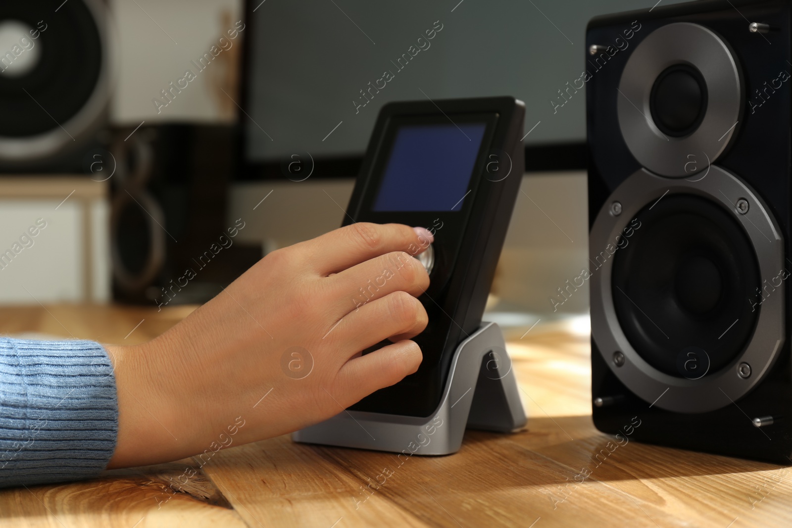 Photo of Woman using remote to control audio speakers at wooden table indoors, closeup