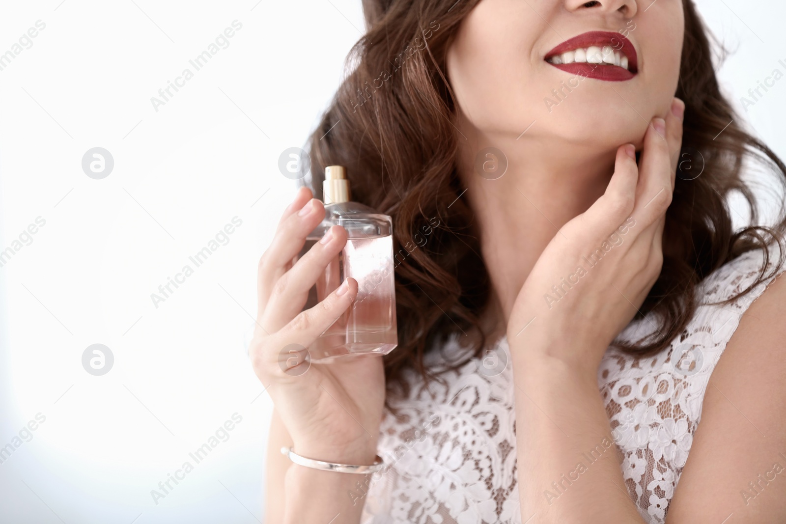 Photo of Beautiful young bride with bottle of perfume on light background, closeup
