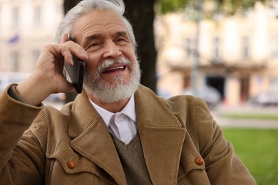 Photo of Handsome senior man talking on smartphone outdoors, space for text