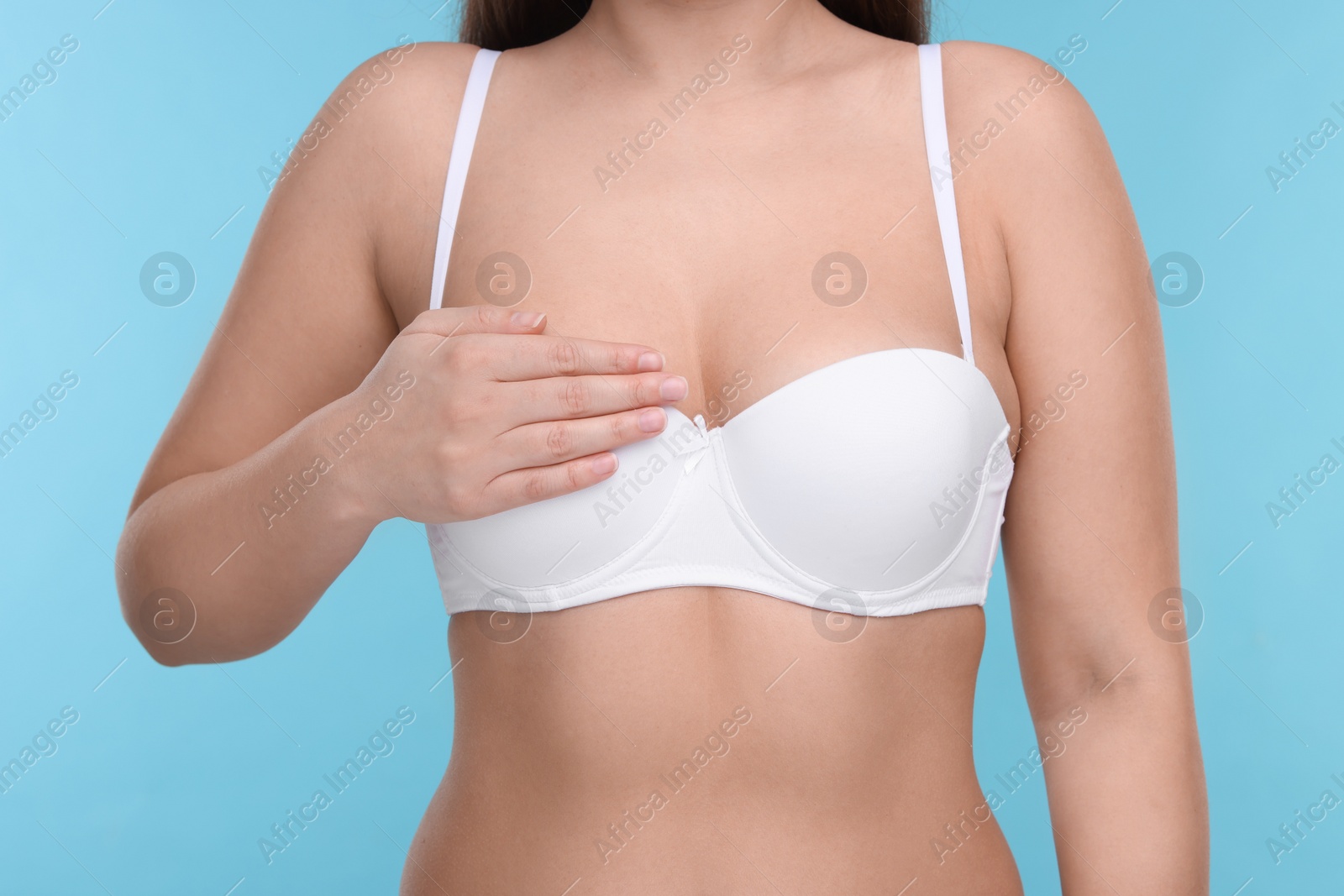 Photo of Mammology. Woman in bra doing breast self-examination on light blue background, closeup