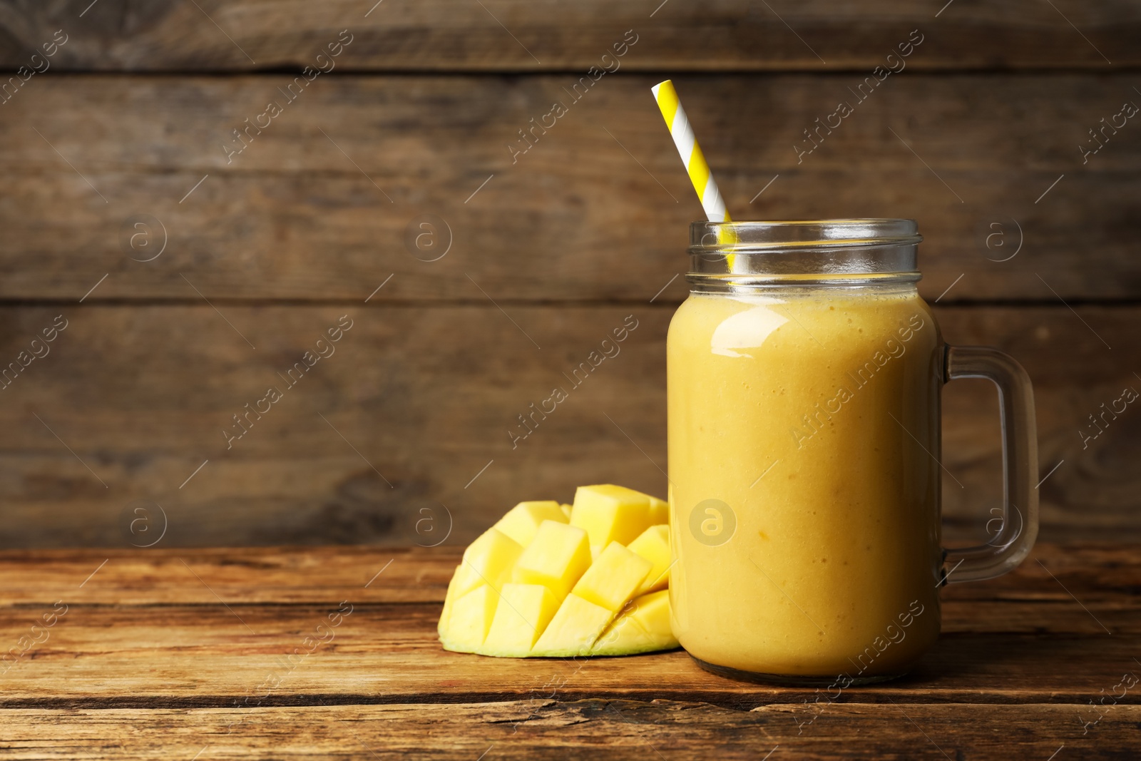 Photo of Mason jar with delicious fruit smoothie and fresh mango on wooden table. Space for text