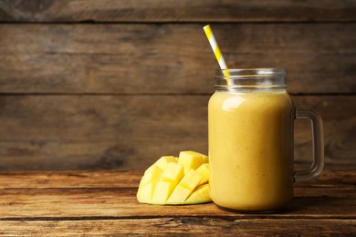 Photo of Mason jar with delicious fruit smoothie and fresh mango on wooden table. Space for text