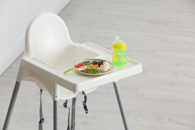 Photo of Baby high chair with healthy food and water indoors