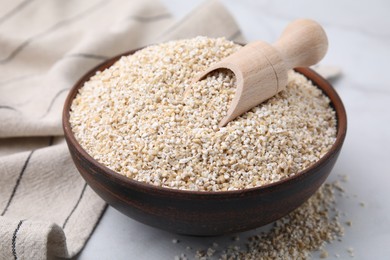 Dry barley groats and scoop in bowl on white table, closeup