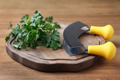 Photo of Cutting board with parsley and mezzaluna knife on wooden table