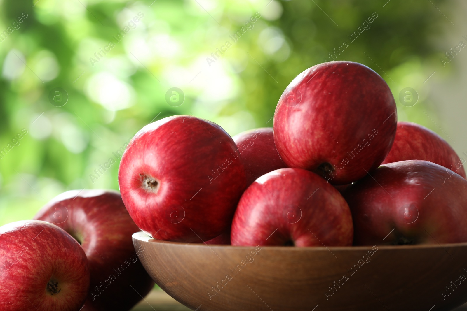Photo of Ripe red apples and bowl on blurred background, closeup