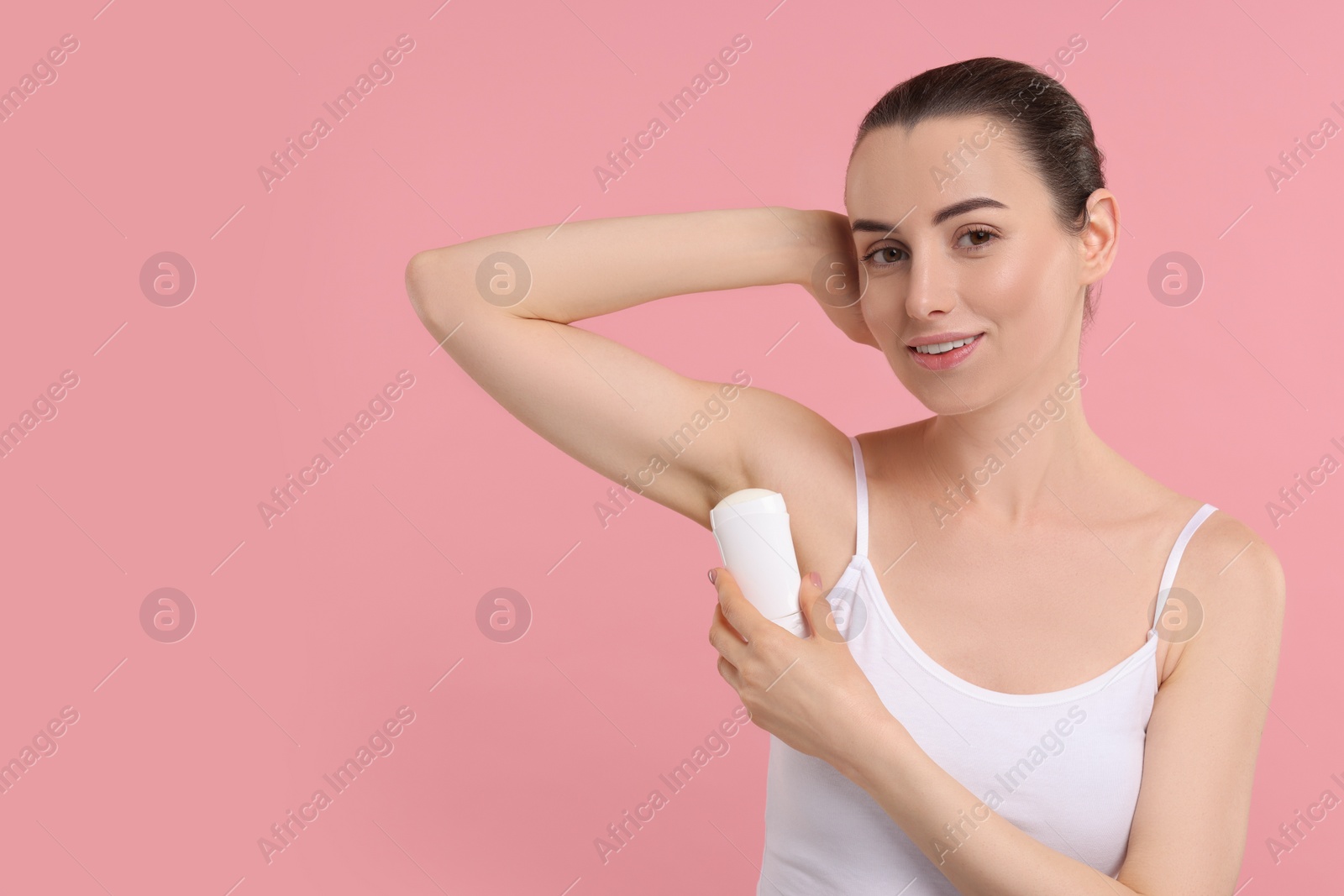 Photo of Beautiful woman applying deodorant on pink background, space for text