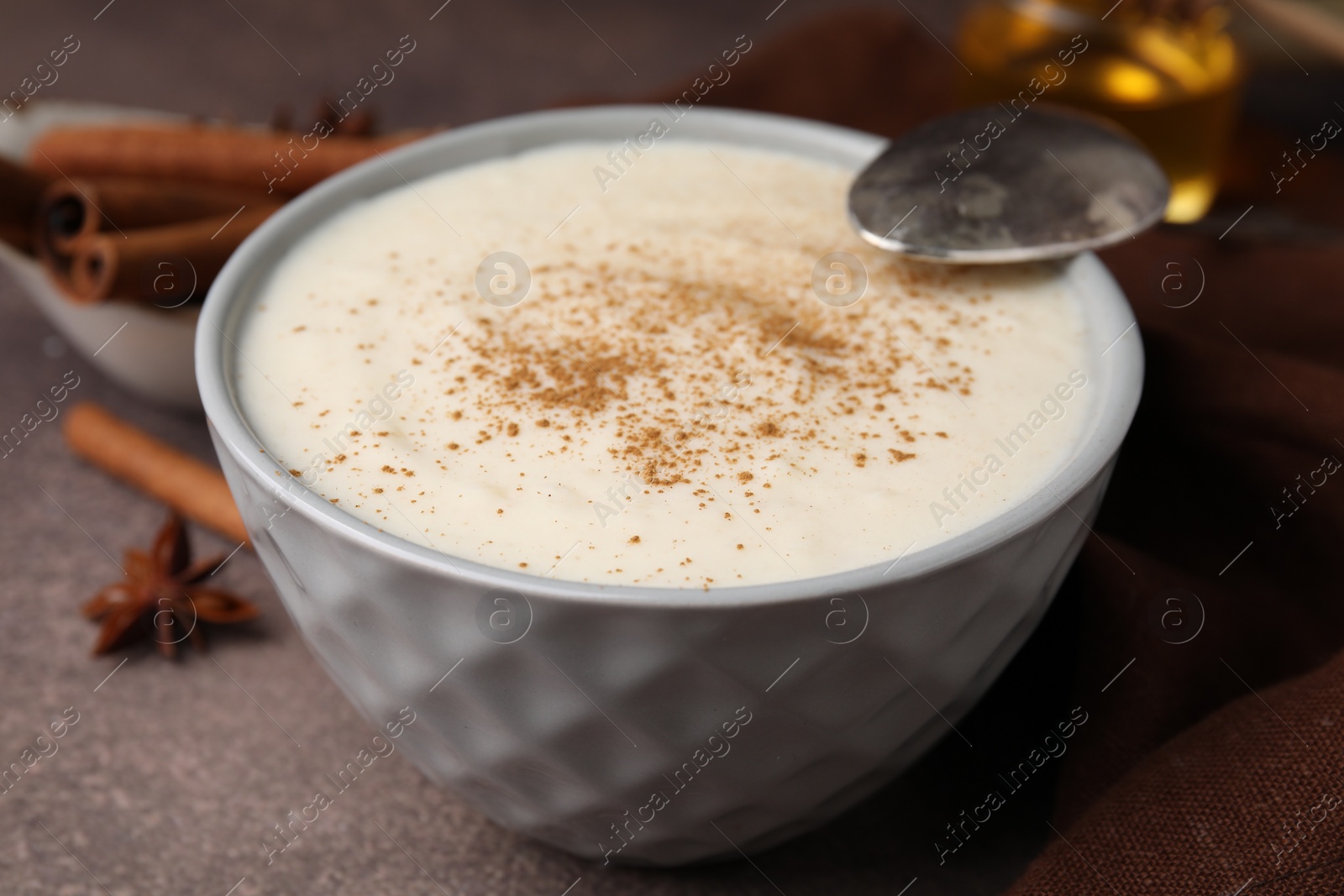 Photo of Delicious semolina pudding with cinnamon in bowl and spoon on brown table, closeup