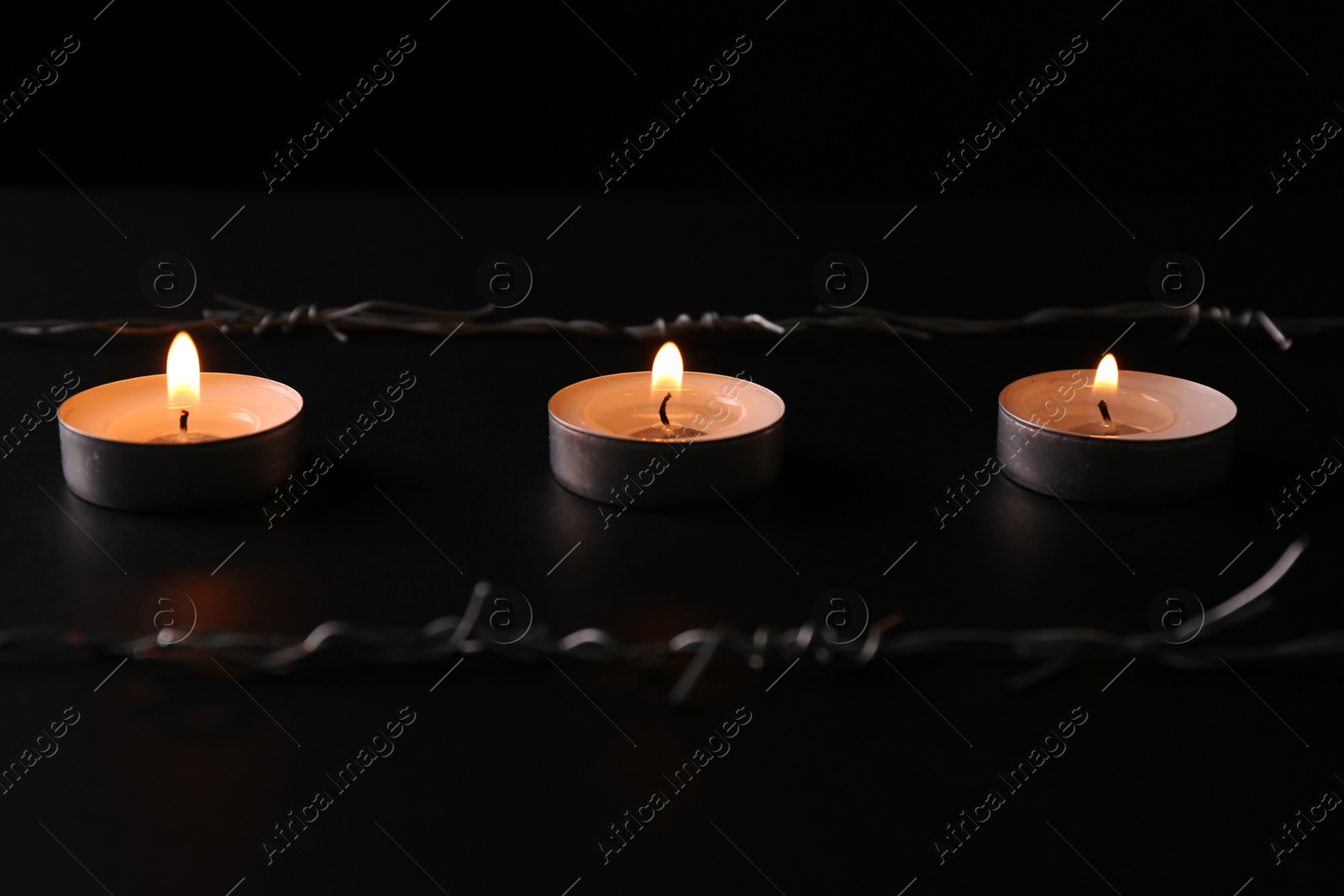 Photo of Burning candles and barbed wire on black background. Holocaust memory day