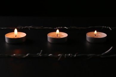 Photo of Burning candles and barbed wire on black background. Holocaust memory day