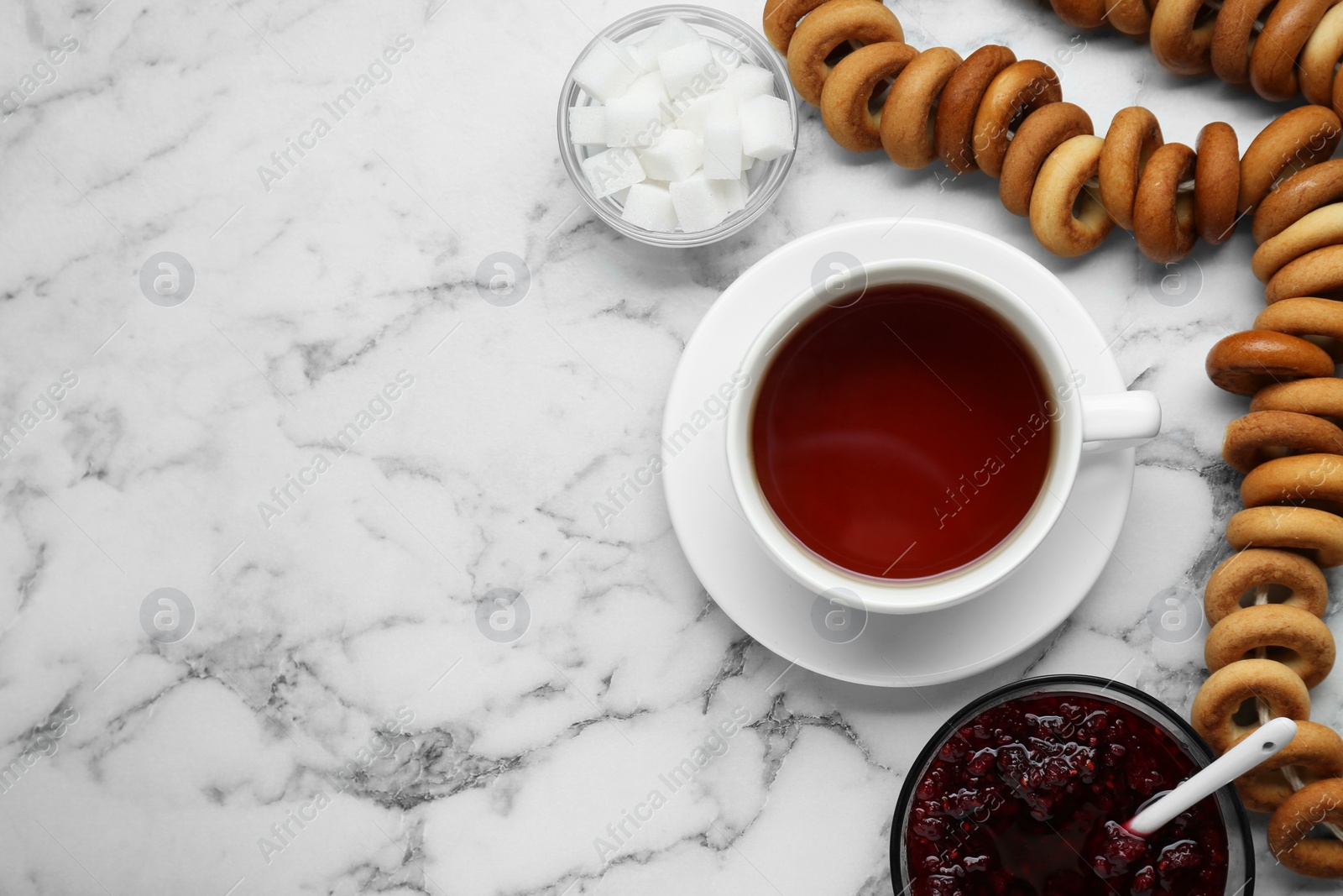 Photo of Flat lay composition with delicious ring shaped Sushki (dry bagels) and cup of tea on white marble table, space for text