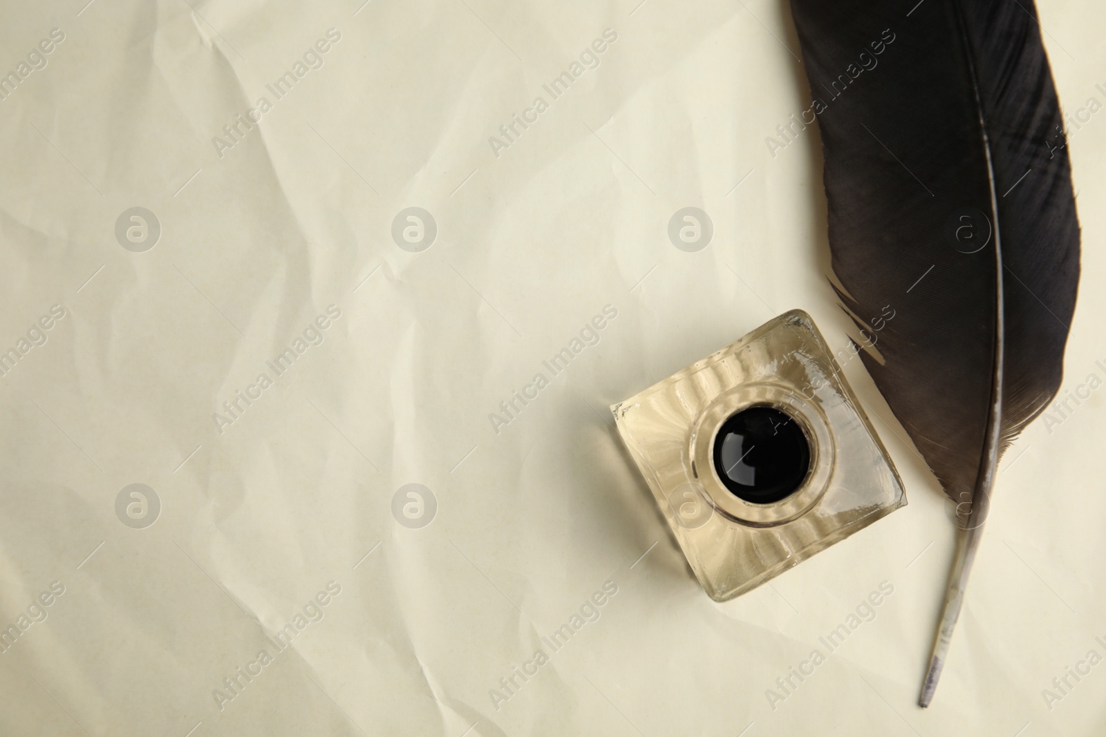 Photo of Feather pen and inkwell on old crumpled paper, flat lay. Space for text