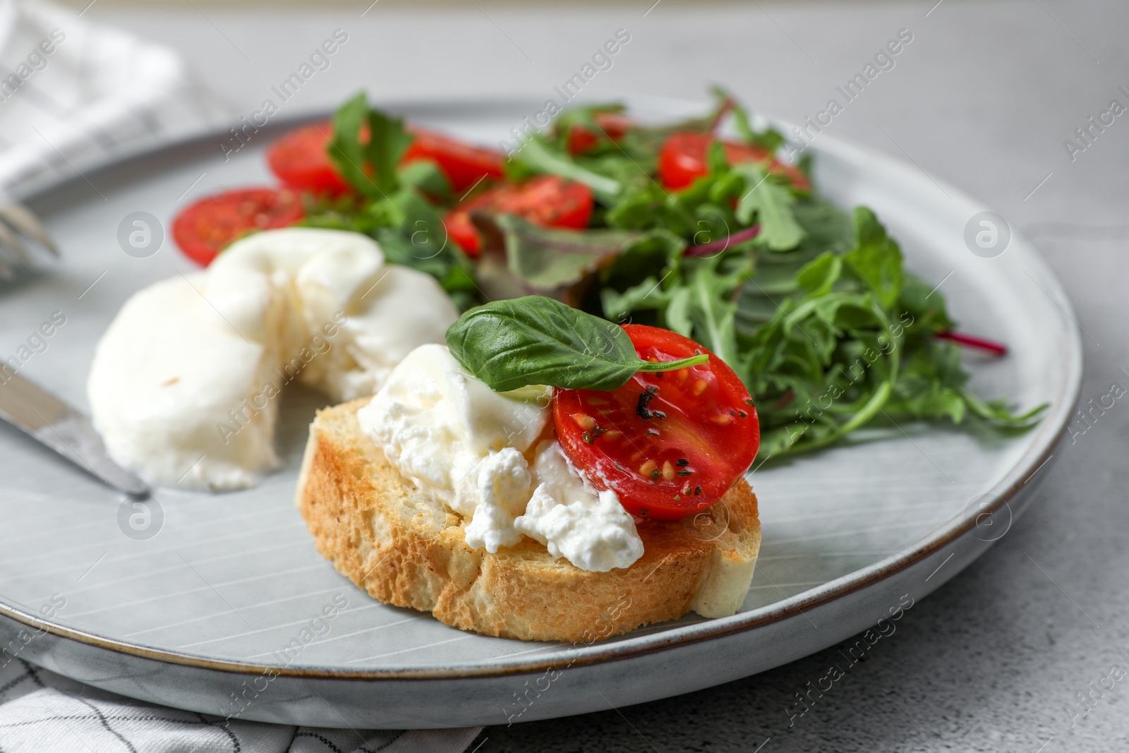 Photo of Delicious burrata cheese with tomatoes, arugula and toast on grey table, closeup