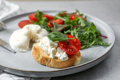 Delicious burrata cheese with tomatoes, arugula and toast on grey table, closeup