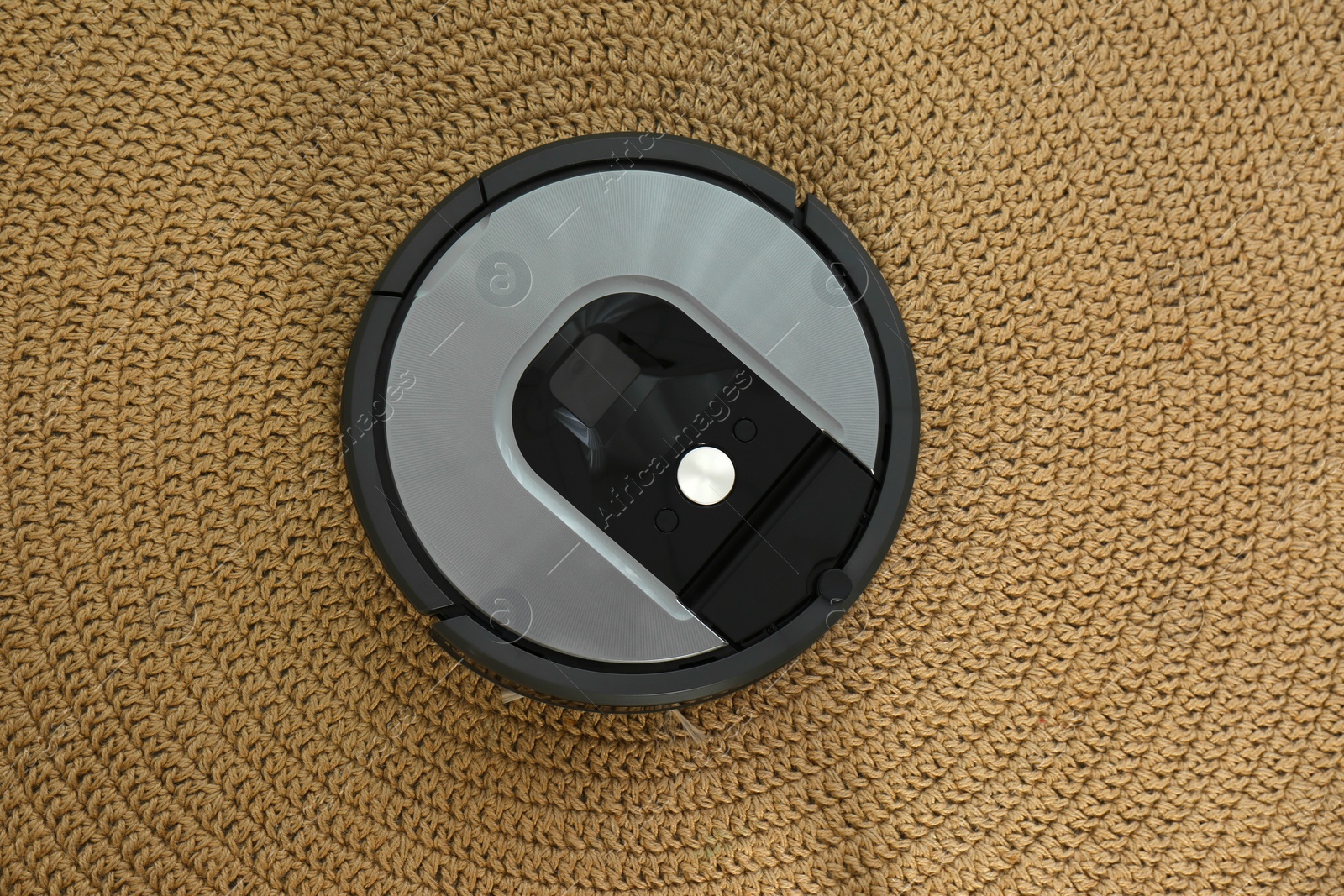 Photo of Modern robotic vacuum cleaner on knitted rug, top view