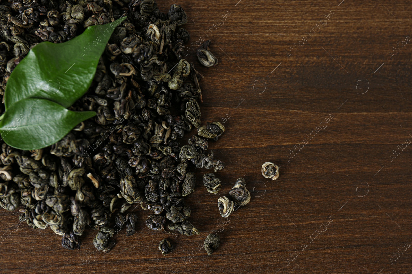 Photo of Heap of dried green tea leaves on wooden table, top view. Space for text