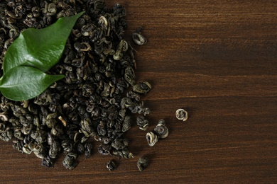 Photo of Heap of dried green tea leaves on wooden table, top view. Space for text