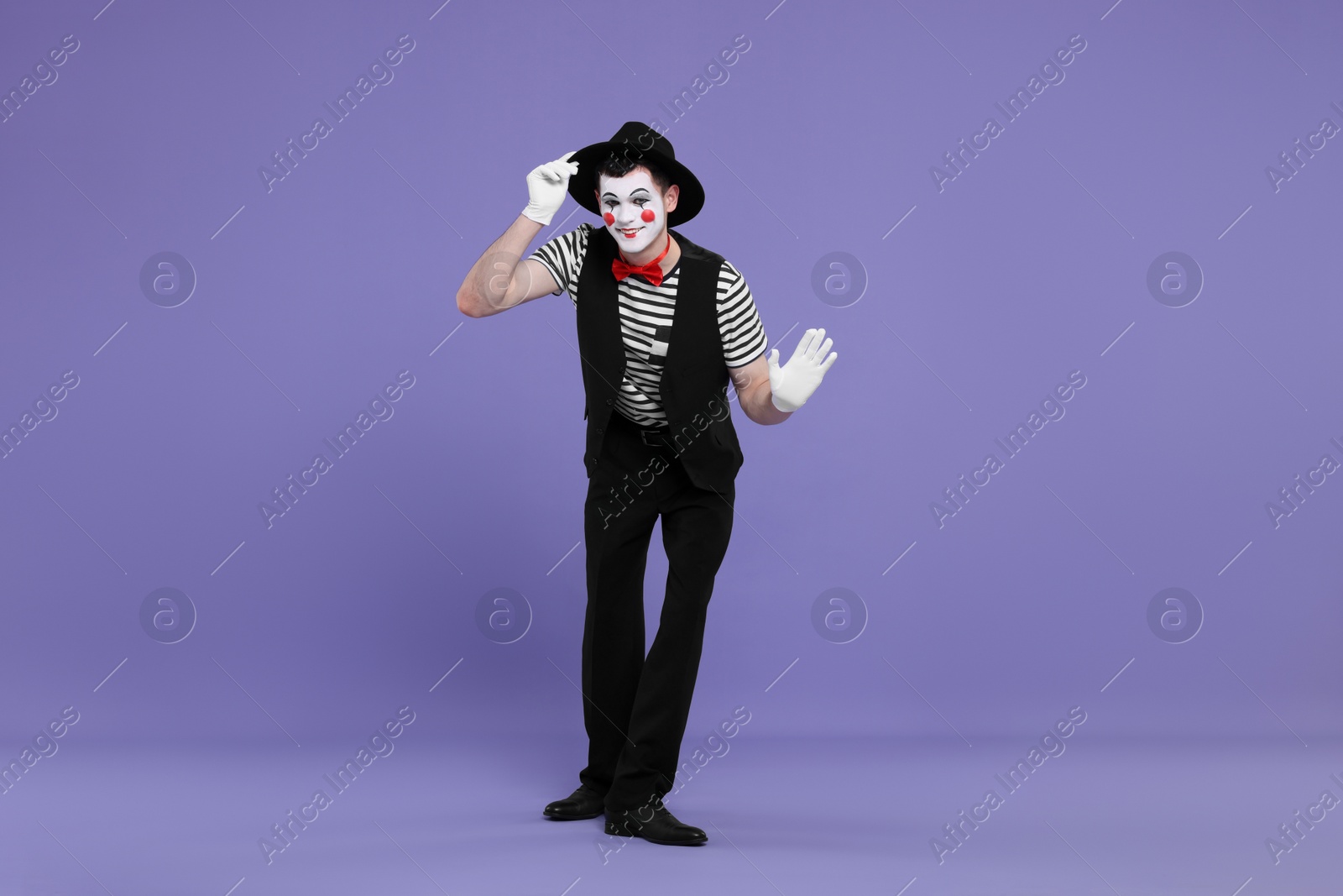 Photo of Funny mime artist in hat posing on purple background