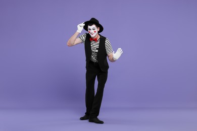 Funny mime artist in hat posing on purple background