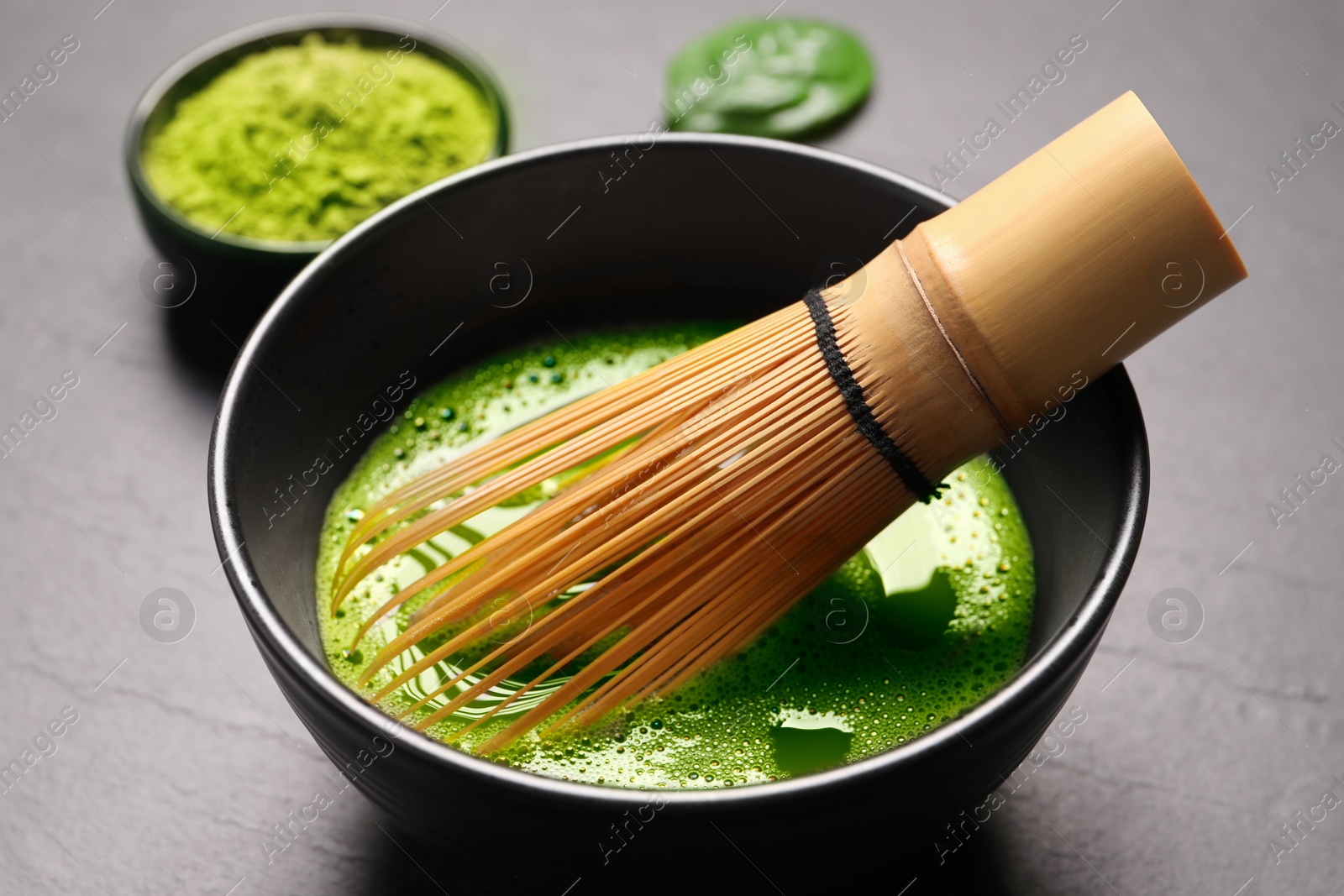 Photo of Cup of matcha tea and bamboo whisk on gray table, closeup