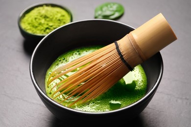 Cup of matcha tea and bamboo whisk on gray table, closeup