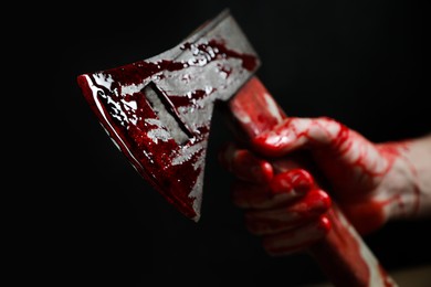Man holding bloody axe on black background, closeup