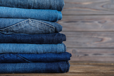 Photo of Stack of different jeans on wooden table, closeup