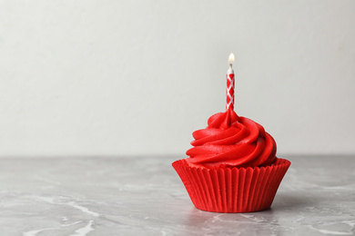 Photo of Delicious birthday cupcake with cream and burning candle on marble table. Space for text