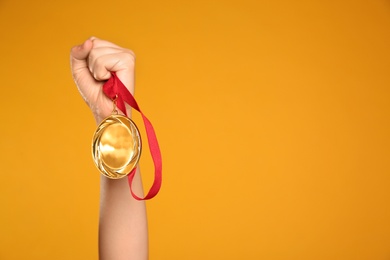 Woman holding gold medal on yellow background, closeup. Space for text