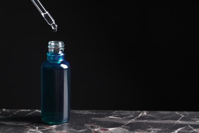 Dripping cosmetic serum from pipette into bottle on grey marble table, space for text